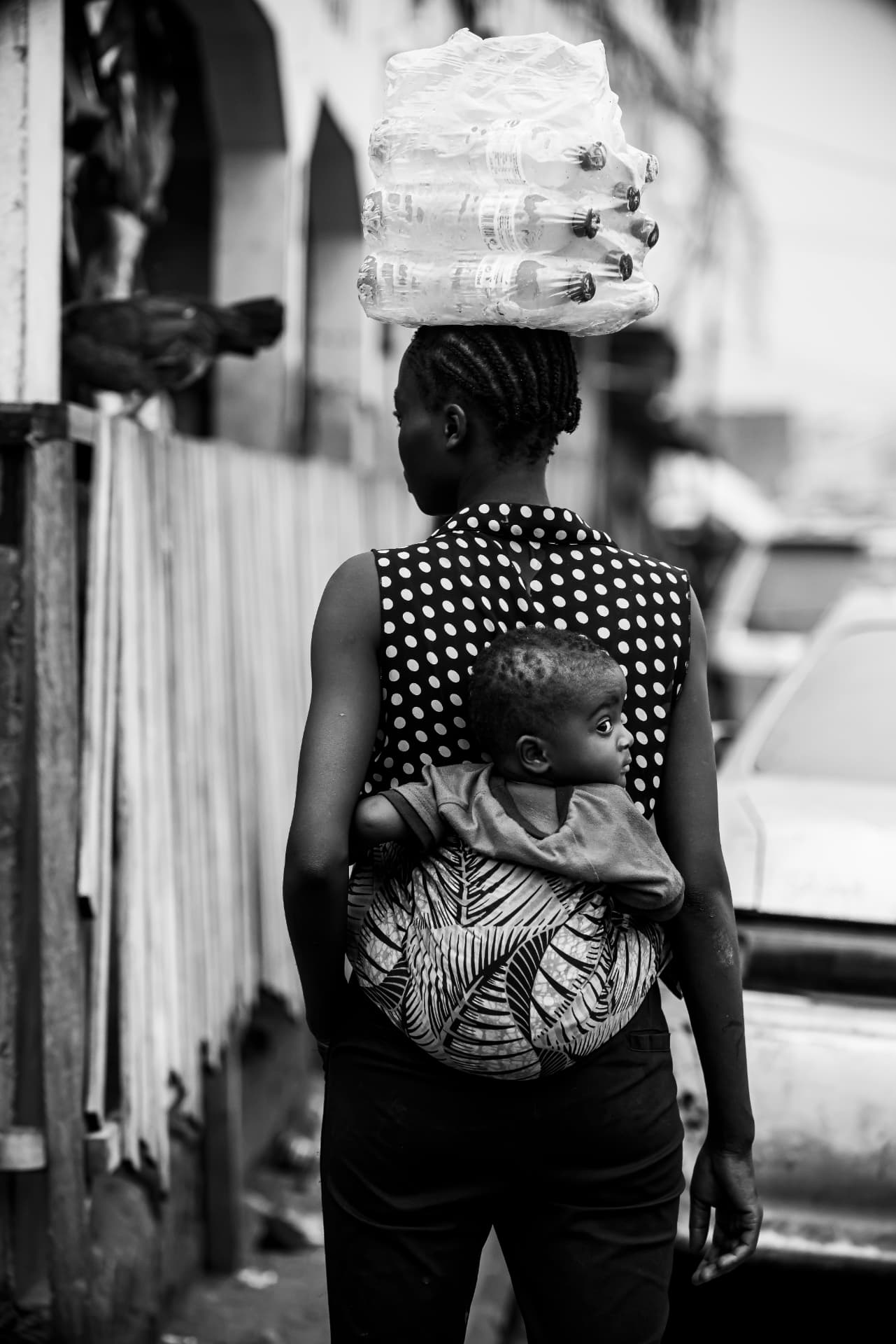 Une femme porte un paquet de bouteilles sur la tête et un enfant dans le dos