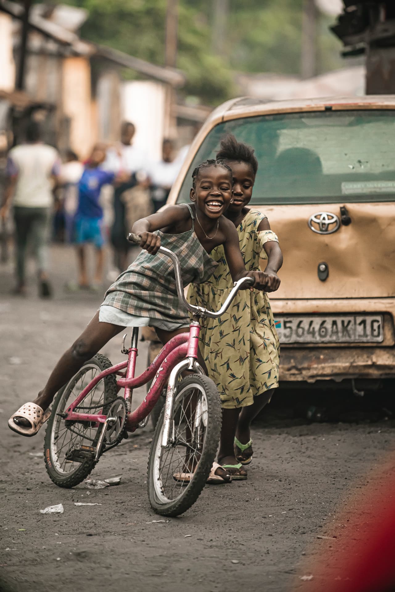 Deux fillettes rieuses partageant un vélo rouge dans une rue de Kinshasa