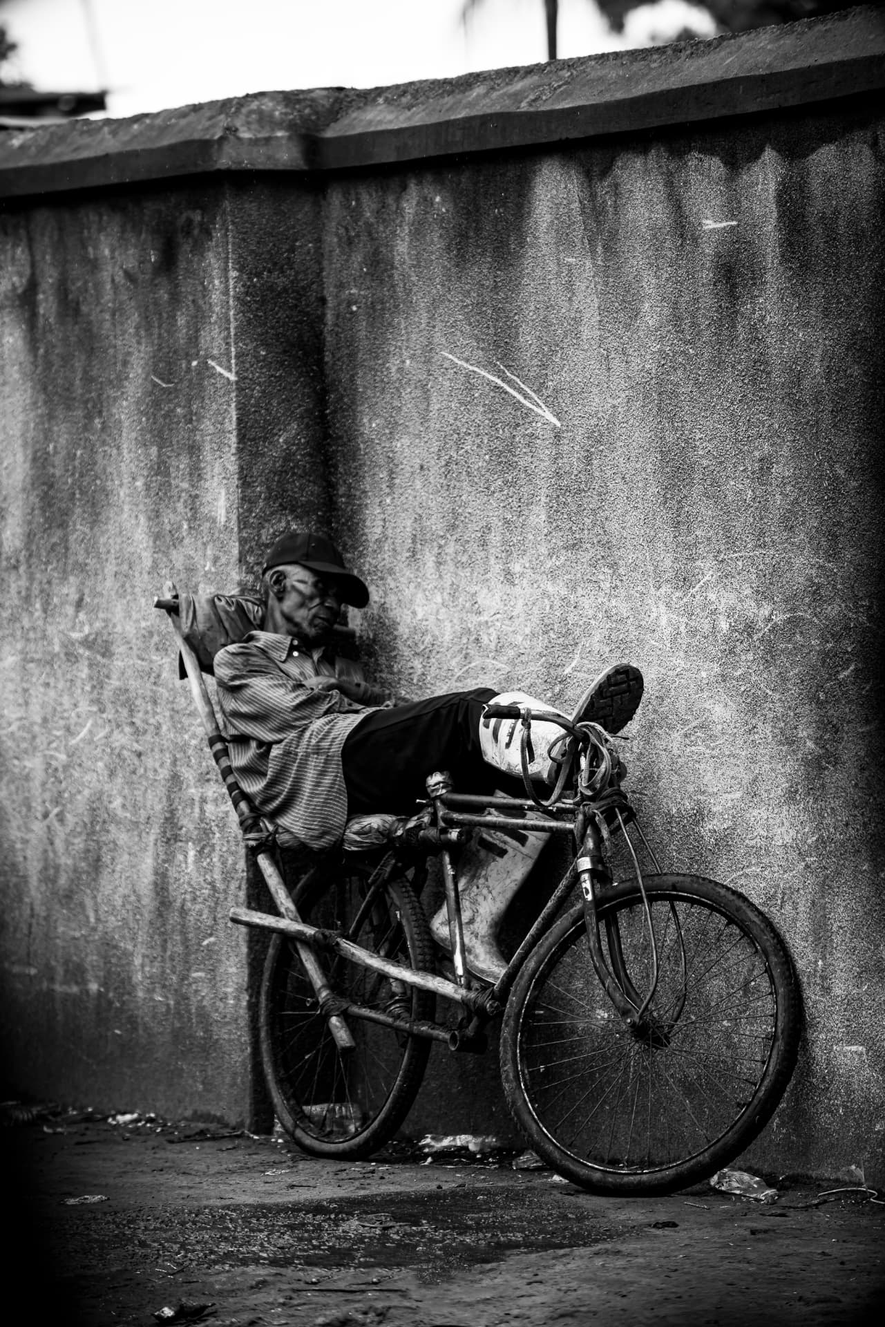 Un homme âgé se repose allongé sur son vélo contre un mur