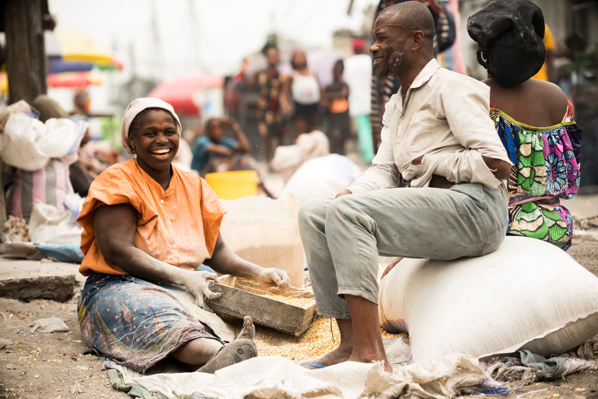 Vendeuse souriante tamisant le maïs au marché, entourée de clients
