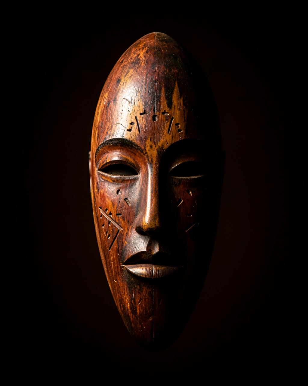 Masque africain en bois sculpté, éclairé sur fond noir